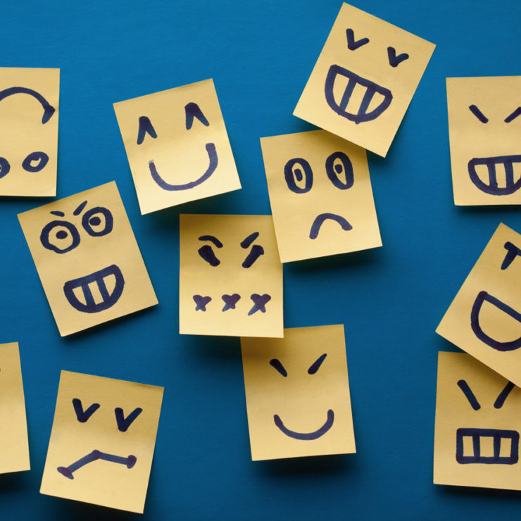 Yellow sticky notes on a blue wall with different emotion expressions demonstrating that people experience may different emotions