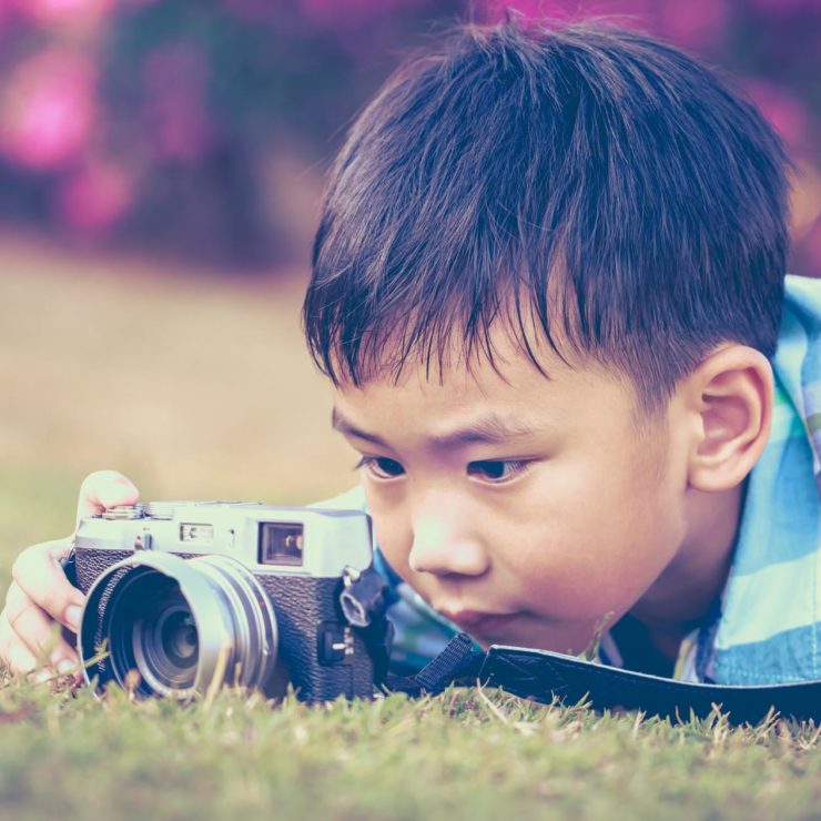 Young boy lying on his stomach and taking a photograph. Image shows how photography can be leveraged as a mindfulness technique.