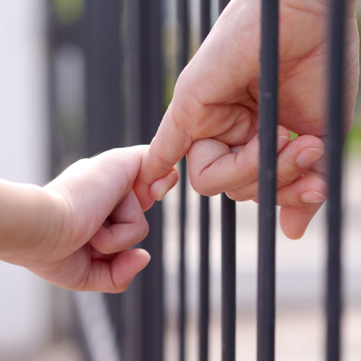Parent And Child Linking Hands Through Bars