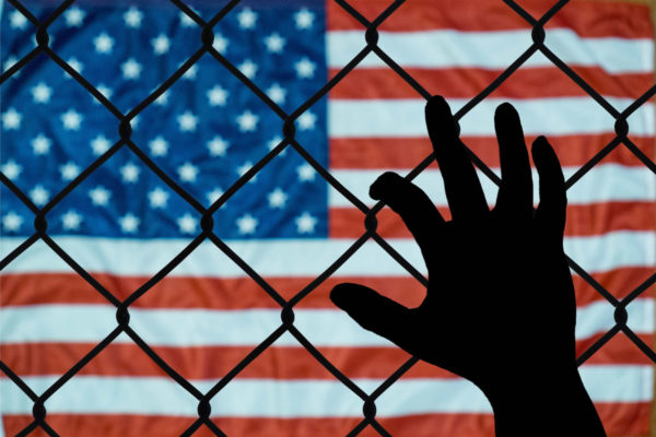 Silhouette Of Hand On Fence With American Flag In The Background To Depict Parent Child Separation At The Mexico Us Border