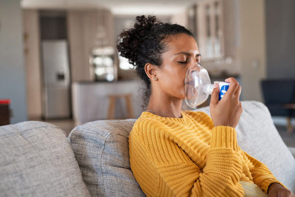 Woman Using Inhaler Sitting On Couch